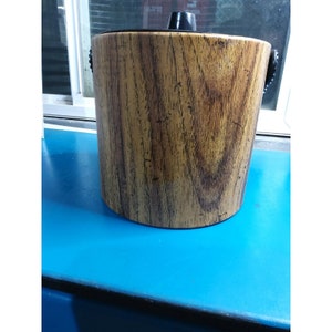 May include: A wooden ice bucket with black handles. The bucket has a wood grain pattern.