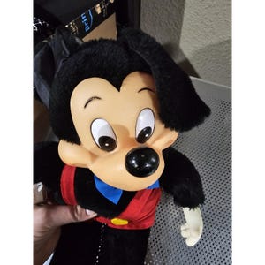 Pu&ograve; includere: Giocattolo di peluche Mickey Mouse nero e rosso con un papillon blu. Il giocattolo ha una testa grande con orecchie nere e un naso marrone.