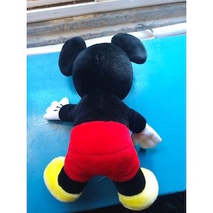 Może przedstawiać: Pluszowa zabawka Mickey Mouse w kolorze czarnym i czerwonym z ż&oacute;łtymi butami. Zabawka jest odwr&oacute;cona tyłem do kamery.