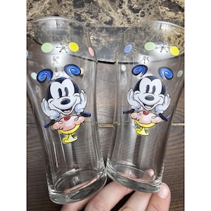 May include: Two clear glass Mickey Mouse drinking glasses with colorful polka dots and a cartoon image of Mickey Mouse holding a sundae.