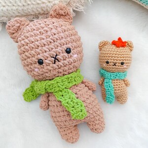 Puede incluir: Dos osos de peluche de crochet con bufandas. El oso más grande es marrón con una bufanda verde y el oso más pequeño es marrón con una bufanda azul.