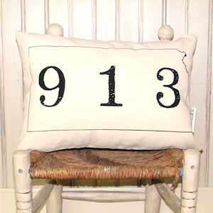 May include: A white pillow with black text that reads "913" on a white painted wooden chair with a woven straw seat.