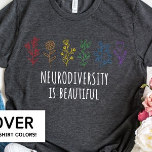 May include: A dark gray t-shirt with a white graphic design featuring a row of colorful flowers and the text "Neurodiversity is beautiful".
