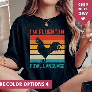 May include: A black t-shirt with a retro-style graphic of a rooster and the text "I'm fluent in fowl language".