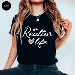 May include: Black t-shirt with the text "Realtor life" in white cursive font. A pink house with a key is above the word "Realtor". A heart with a leopard print pattern is to the left of the word "life".