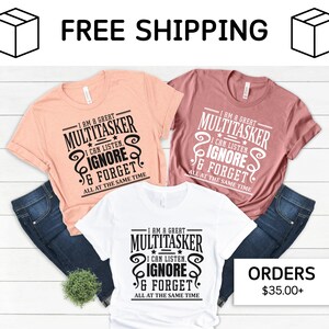 May include: Three t-shirts with a humorous saying about multitasking. The shirts are in white, peach, and pink. The text on the shirts reads "I am a great multitasker. I can listen, ignore, and forget all at the same time."