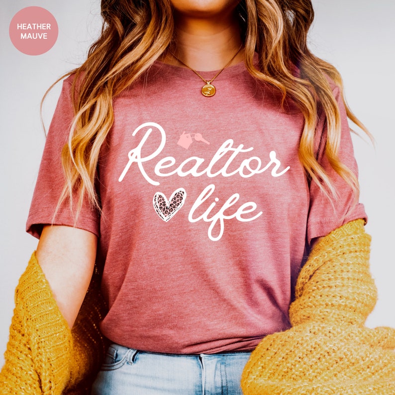 May include: A heather mauve t-shirt with the text "Realtor life" in white script. A pink heart with a leopard print design is next to the word "life".