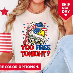May include: White t-shirt with a cartoon bald eagle wearing sunglasses and a red, white, and blue bandana. The eagle has a red beak and yellow eyes. The text "You Free Tonight?" is printed below the eagle.