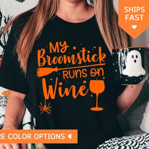 May include: Black t-shirt with orange text that reads "My Broomstick Runs on Wine" with a graphic of a broom, stars, and a wine glass.