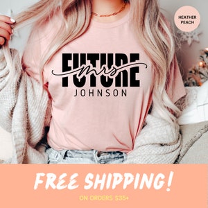 May include: A pink t-shirt with the text "Future Mrs. Johnson" in black lettering. The shirt is being worn by a person with long blonde hair. The text "Free Shipping! On orders $35+" is at the bottom of the image.