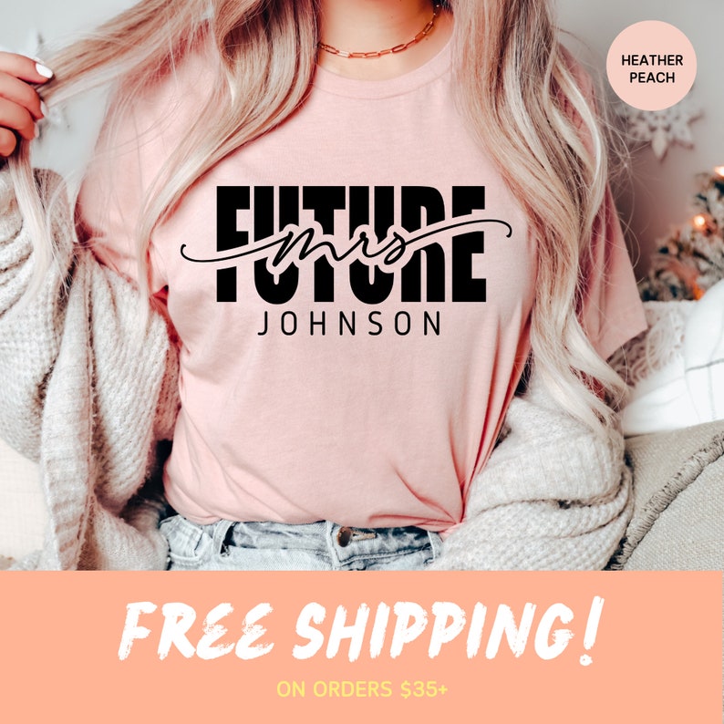 May include: A pink t-shirt with the text "Future Mrs. Johnson" in black lettering. The shirt is being worn by a person with long blonde hair. The text "Free Shipping! On orders $35+" is at the bottom of the image.