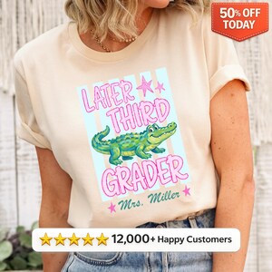 Könnte beinhalten: Beiges T-Shirt mit dem Text "Later Third Grader" und einem Cartoon-Alligator. Das Design beinhaltet rosa Sterne und blaue Streifen. Der Text "Mrs. Miller" ist ebenfalls enthalten. Ein rot-weißes "50% OFF TODAY"-Etikett befindet sich oben rechts.