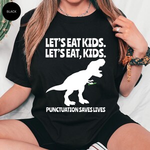 Puede incluir: Camiseta negra con un gr&aacute;fico de dinosaurio blanco y el texto "Let's eat kids. Let's eat, kids. Punctuation saves lives."