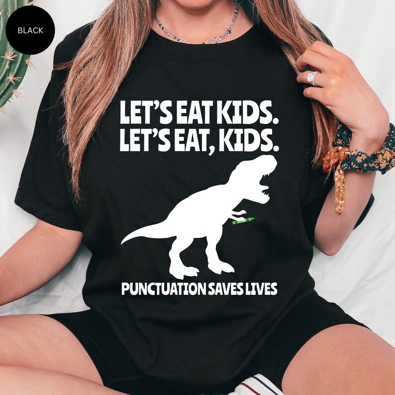 Puede incluir: Camiseta negra con un gr&aacute;fico de dinosaurio blanco y el texto "Let's eat kids. Let's eat, kids. Punctuation saves lives."