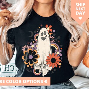 May include: Black t-shirt with a white ghost wearing a smile and surrounded by colorful flowers and stars. The ghost is in a retro style with a rainbow behind it.