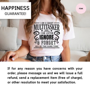 May include: A white t-shirt with black text that reads "I am a great multitasker. I can listen, ignore & forget. All at the same time." The shirt is being worn by a person sitting on a couch. The text "Happiness Guarantee!" is in the top left corner of the image. The text "Pink" is in the top right corner of the image.