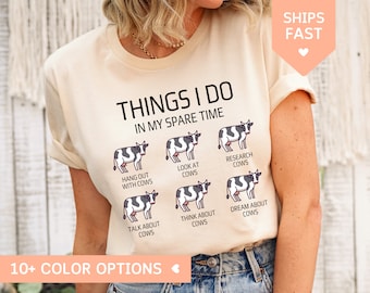 May include: A beige t-shirt with the text "Things I do in my spare time" and a graphic of six cows with different activities, including "Hang out with cows", "Look at cows", "Research cows", "Talk about cows", "Think about cows", and "Dream about cows".