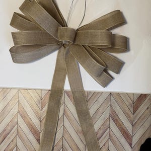 May include: A large brown burlap bow with long tails. The bow is tied with a wire.
