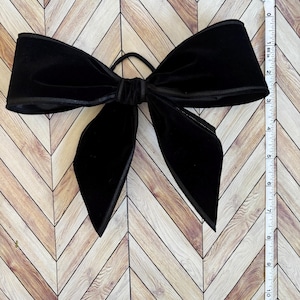May include: A large black velvet bow with a satin edge. The bow is tied with a black elastic band.