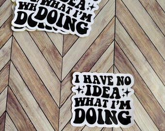 Op de afbeelding: Een witte sticker met zwarte tekst die "Ik heb geen idee wat ik doe" zegt met een ster aan weerszijden van het woord "idee".