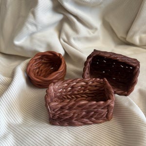 以下が含まれることがあります： 茶色のロープで編まれた3つのバスケット。バスケットはサイズと形が異なります。一番大きなバスケットは長方形、中くらいのバスケットは丸型、一番小さなバスケットは小さな正方形です。