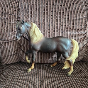 May include: A dark brown horse figurine with a cream-colored mane and tail. The horse is depicted in a standing position with one front leg slightly raised. It features a white blaze on its face and light brown lower legs with dark hooves.