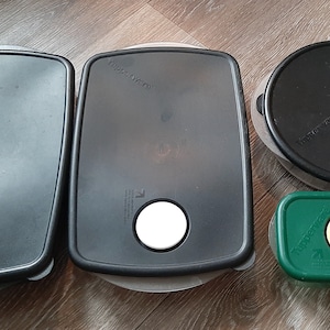 May include: Four Tupperware food storage containers with lids. Two large rectangular black containers feature red and white circular vents. One medium round black container has a white vent. One small green rectangular container has a yellow vent.