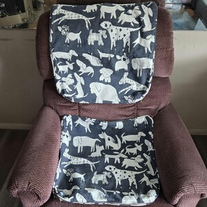 May include: A dark blue chair cover set with a white dog pattern. The set includes a headrest cover and a seat cover, both featuring various dog breeds in a repeating design. The covers are placed on a maroon corduroy recliner.