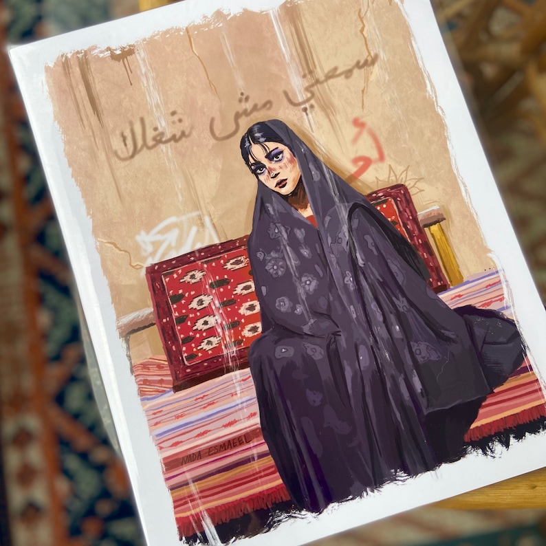 May include: A woman wearing a dark purple headscarf sits on a patterned rug. The wall behind her is beige with faded writing in Arabic. The writing says "سعيي مشي شعاع".