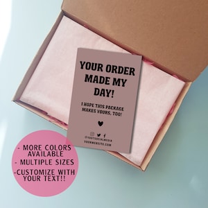 May include: A brown cardboard box with a pink tissue paper lining. The box contains a card with the text "YOUR ORDER MADE MY DAY! I HOPE THIS PACKAGE MAKES YOURS, TOO!" and social media information. The card is next to a pink circle with the text "MORE COLORS AVAILABLE - MULTIPLE SIZES - CUSTOMIZE WITH YOUR TEXT!!"