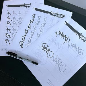 May include: Four sheets of white paper with black ink lettering and designs. The sheets feature various letter styles and a signature. A black marker pen rests on the bottom left corner of the papers. The papers are on a dark surface.