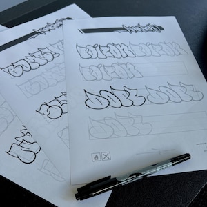 May include: Several sheets of paper with graffiti lettering practice. The sheets feature outlines and examples of stylized words. A black marker with silver accents lies on the paper. The text on the marker reads "David Koslowski".