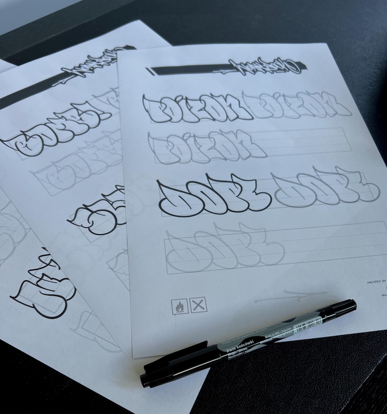 May include: Several sheets of paper with graffiti lettering practice. The sheets feature outlines and examples of stylized words. A black marker with silver accents lies on the paper. The text on the marker reads "David Koslowski".