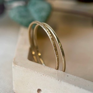 May include: Two gold-toned metal rings stacked on top of each other, resting on a light beige concrete tray with a cork border.