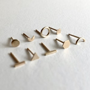 May include: A set of nine gold-toned stud earrings featuring different geometric shapes, including a circle, square, hexagon, crescent moon, triangle, and a line.