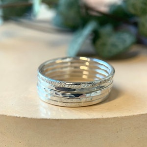 May include: A set of four silver stacking rings. The rings are all different widths and have a hammered texture. The top ring has a textured edge.