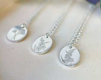 Puede incluir: Tres collares de plata con colgantes ovalados que presentan delicados diseños florales. Cada colgante tiene un motivo floral diferente, mostrando detalles intrincados.