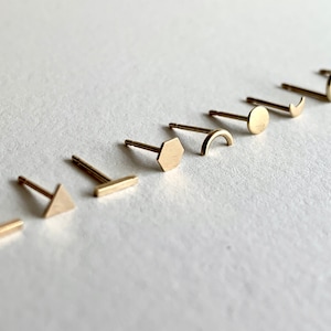 May include: A set of ten gold-toned earrings with different geometric shapes, including a circle, a crescent moon, a hexagon, a rectangle, a triangle, and a curved line.