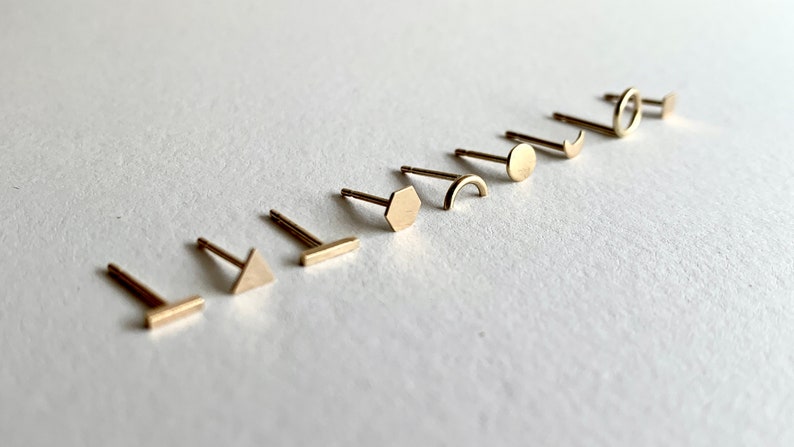May include: A set of ten gold-toned earrings with different geometric shapes, including a circle, a crescent moon, a hexagon, a rectangle, a triangle, and a curved line.