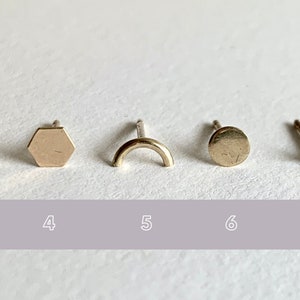 May include: Nine gold geometric stud earrings, each with a different shape: a bar, a triangle, a bar, a hexagon, a crescent, a circle, a crescent, a circle, and a square.