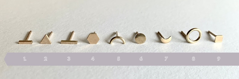 May include: Nine gold geometric stud earrings, each with a different shape: a bar, a triangle, a bar, a hexagon, a crescent, a circle, a crescent, a circle, and a square.