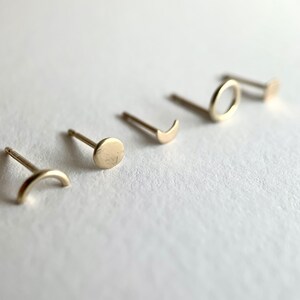 May include: Five gold-toned earrings with different geometric shapes: a circle, a crescent moon, a half-circle, a full circle, and a square.