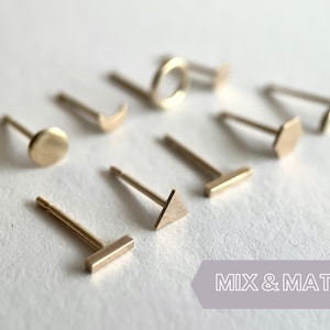May include: A set of gold-toned earrings with different geometric shapes, including a circle, a crescent moon, a triangle, a hexagon, a rectangle, and a circle. The earrings are displayed on a white surface with the text "MIX & MATCH" in the bottom right corner.