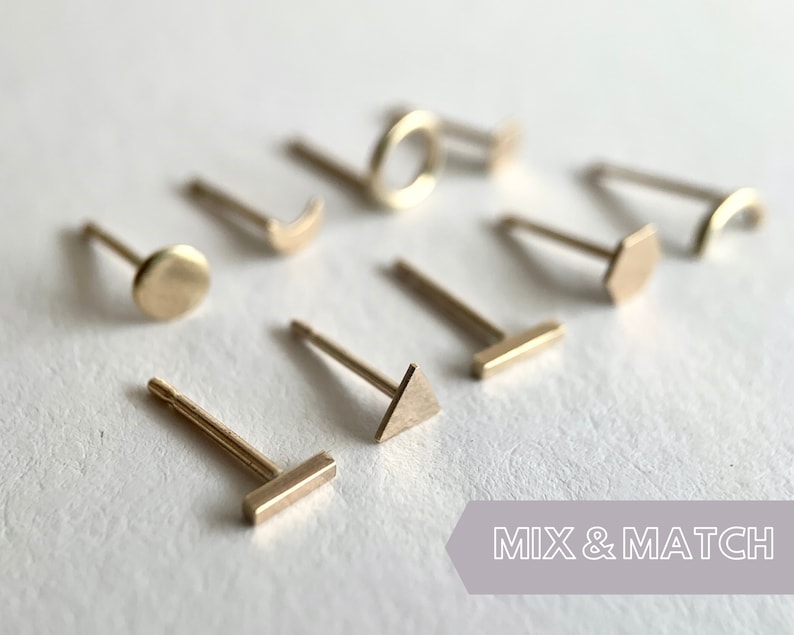 May include: A set of gold-toned earrings with different geometric shapes, including a circle, a crescent moon, a triangle, a hexagon, a rectangle, and a circle. The earrings are displayed on a white surface with the text "MIX & MATCH" in the bottom right corner.