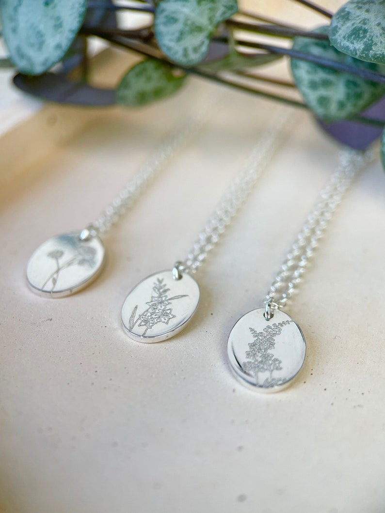 May include: Three silver necklaces with oval pendants featuring delicate floral designs. Each pendant has a different floral motif, showcasing intricate details.