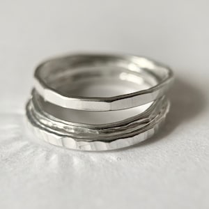 May include: Three silver rings stacked on top of each other. The top ring has a hammered texture, the middle ring has a smooth, slightly rounded texture, and the bottom ring has a textured, ridged surface.
