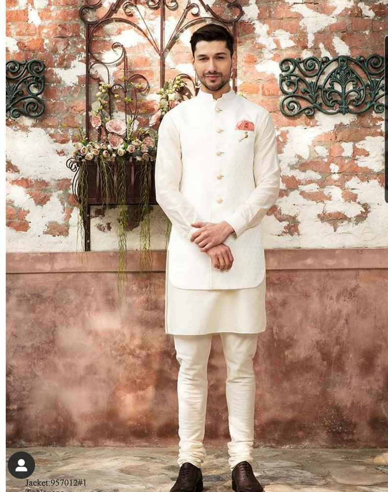Puede incluir: Un hombre con una kurta blanca y un chaleco blanco con estampado floral. Est&aacute; de pie frente a una pared de ladrillo con una maceta colgada.