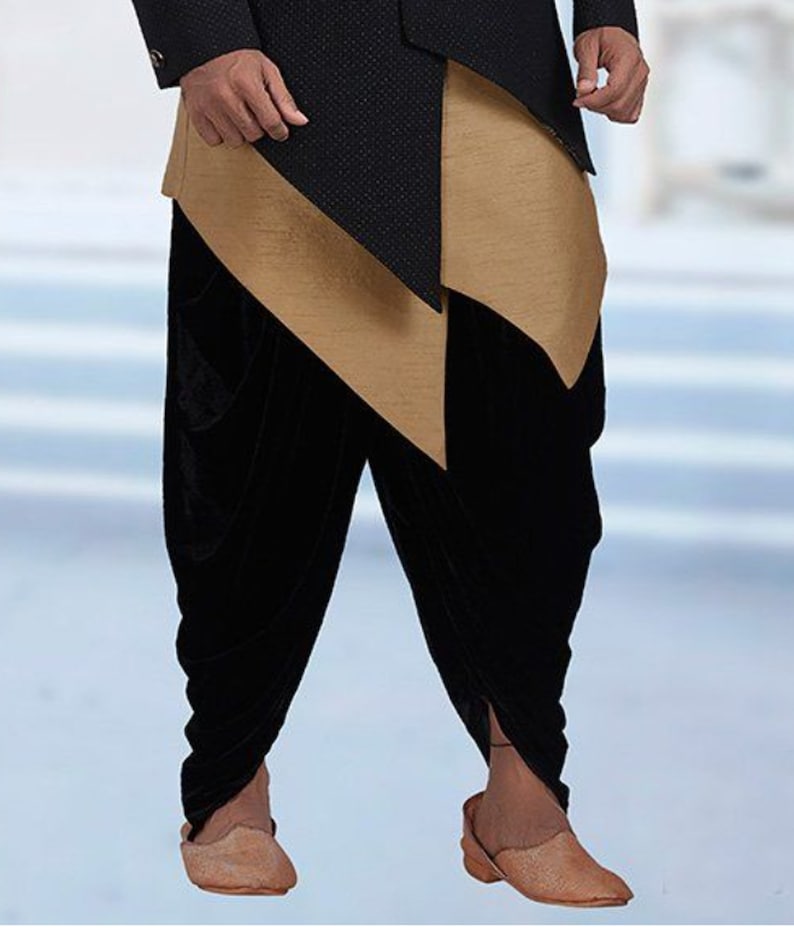 Pu&ograve; includere: Un abito da uomo nero e oro con una parte superiore lunga e asimmetrica e pantaloni di velluto nero. I pantaloni sono raccolti alle caviglie e la parte superiore ha una lunga coda fluida.