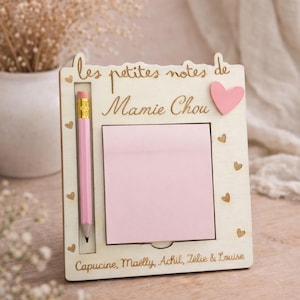 Op de afbeelding: Houten memobord met een roze plakbriefje, een roze potlood en een roze hart. Het bord is gegraveerd met de woorden "les petites notes de Mamie Chou" en de namen Capucine, Maëlly, Achil, Zélie & Louise.
