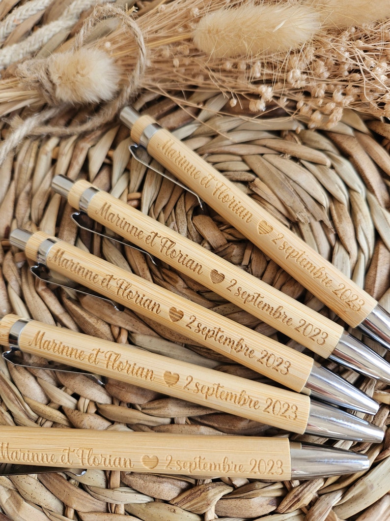 May include: Five wooden pens with silver accents. Each pen is engraved with the text "Marinne et Florian 2 septembre 2023" and a heart symbol.